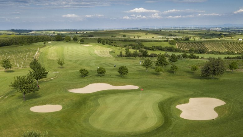 Aerial view of a golf course with green areas, sand bunkers and surrounding fields.