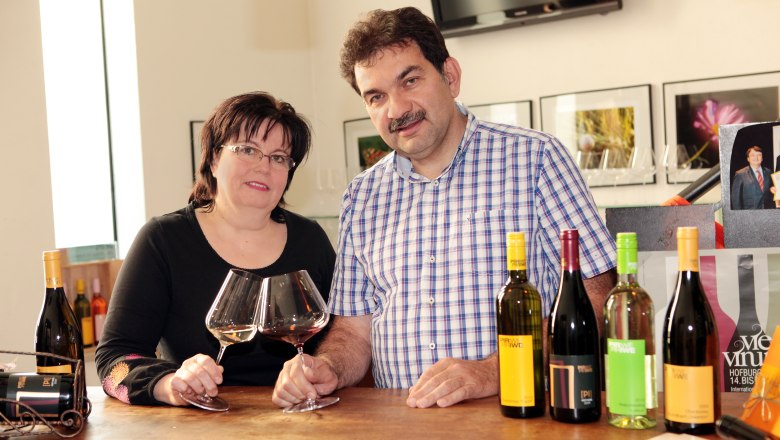 A man and a woman are standing at a table with wine glasses and bottles of wine.
