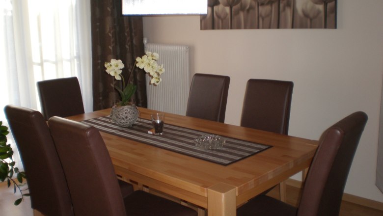 Dining room with wooden table, six brown chairs and orchid as decoration.