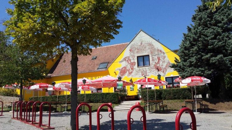 A yellow building with murals, surrounded by trees and red parasols.