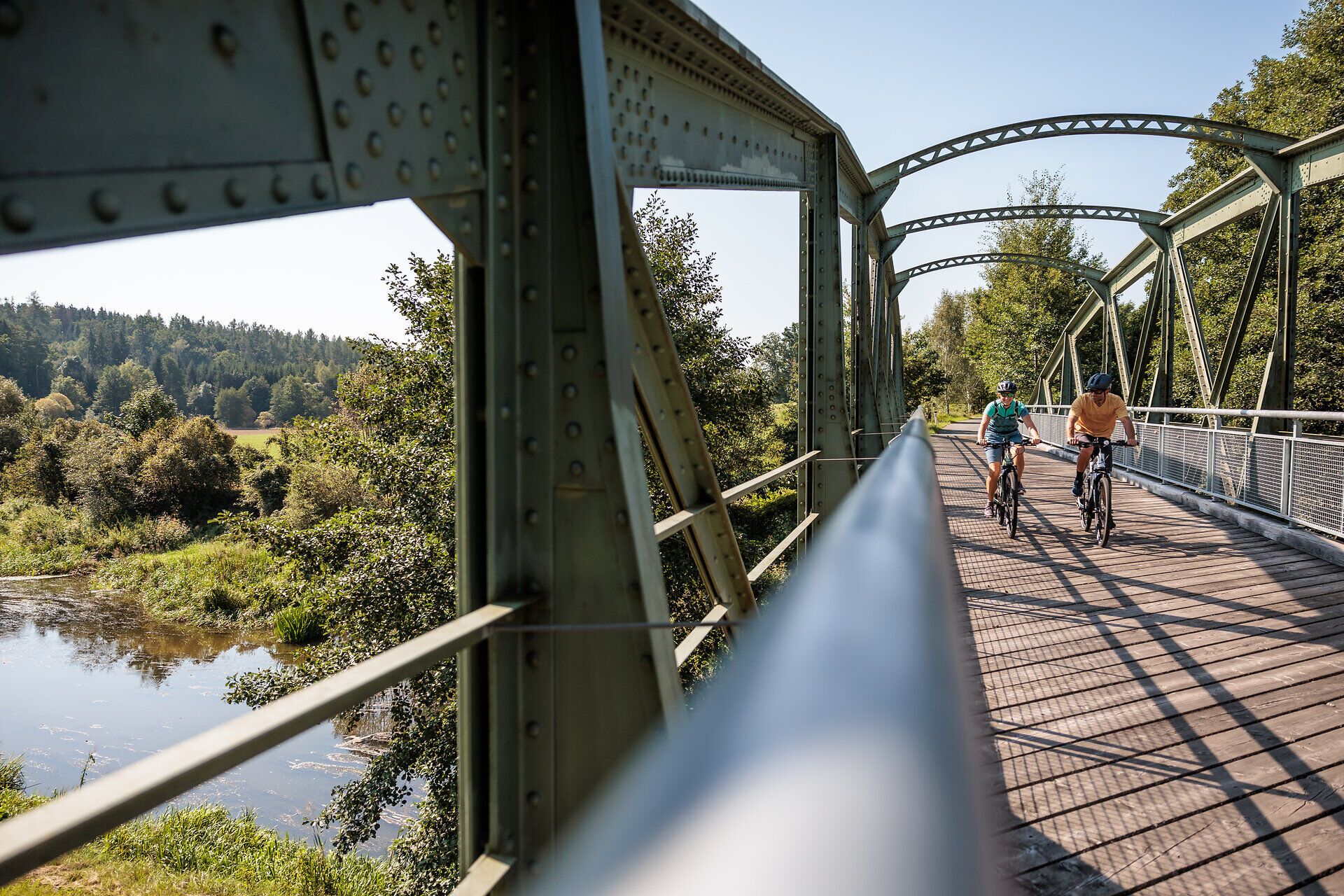 A gentle breeze blows across the Thaya Bridge as cyclists enjoy the picturesque scenery. Surrounded by lush greenery and the gentle lapping of the water, this place invites you to experience the beauty of nature and let your mind wander.