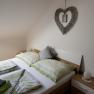 Bedroom with double bed, green bed linen and heart-shaped wall decoration.