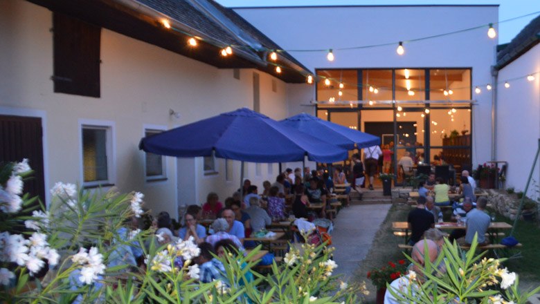 Wine tavern with guests outside, illuminated by fairy lights.
