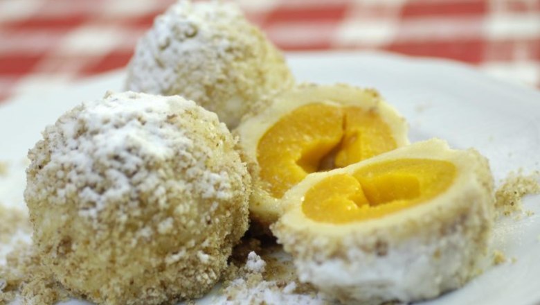 Three apricot dumplings on a plate, one of them sliced