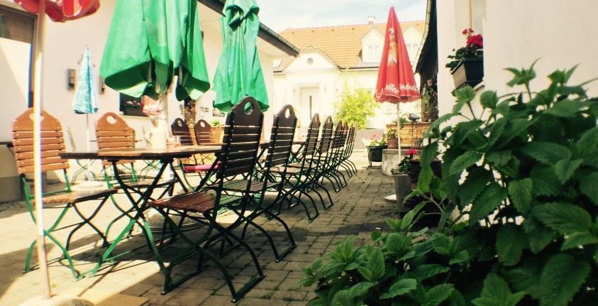 An empty guest garden with wooden tables and chairs, surrounded by green parasols and plants.