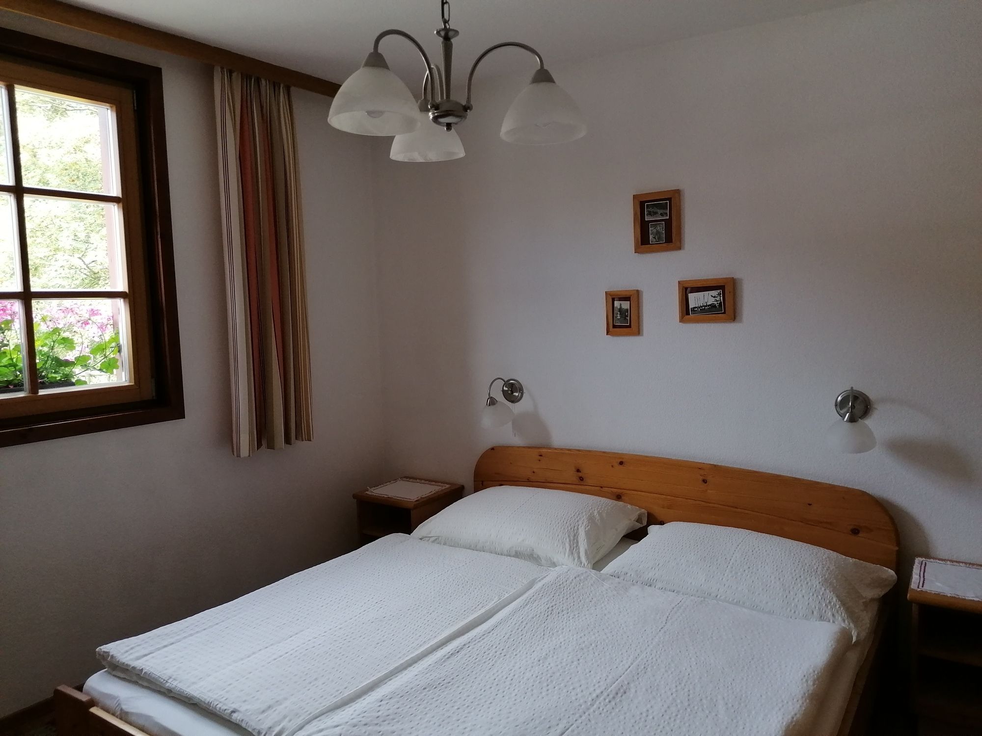 Cozy double room with wooden furniture, a window with curtains and small pictures on the wall.