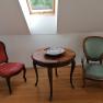 Two antique chairs and a round wooden table with a decorative bowl in a room with a skylight.