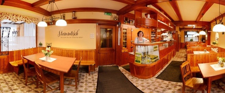 Panorama of a cozy restaurant with wooden furniture and decorative lamps.