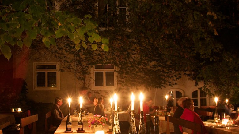 A festively laid table outdoors with candlelight and a buffet of various dishes. People sit at tables in the background.
