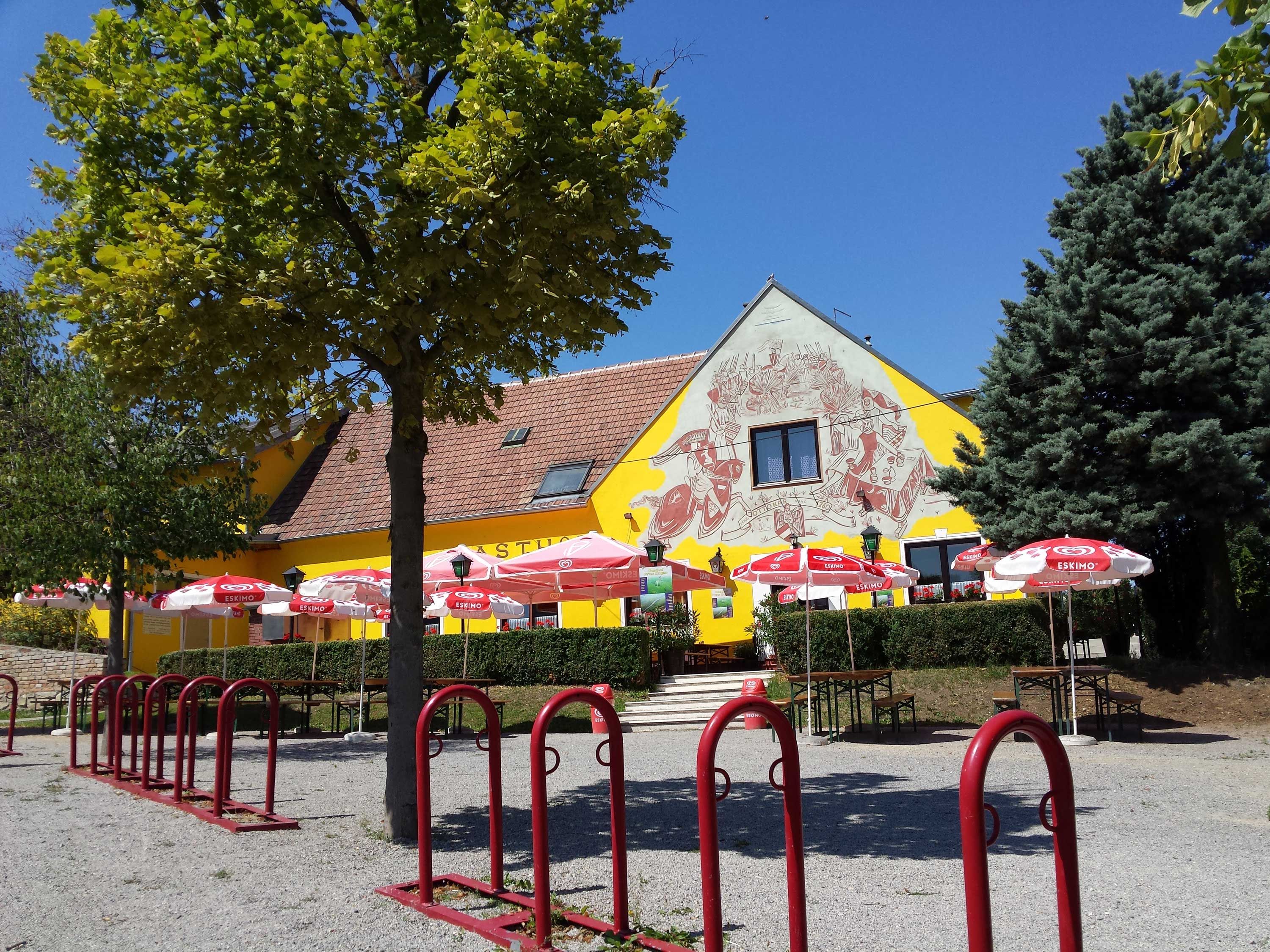 A yellow building with murals, surrounded by trees and red parasols.