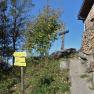 Signpost and wooden cross next to a wooden house in a mountainous landscape.