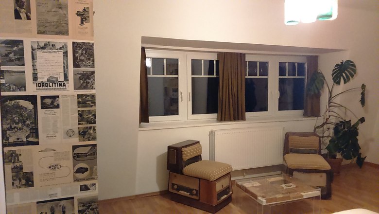 Hotel room with retro furniture, newspaper wall and large plant.