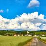 Landscape with village, fields and church in front of large clouds.