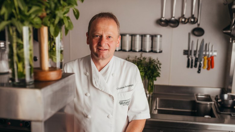 A chef in a white uniform stands in a professional kitchen.