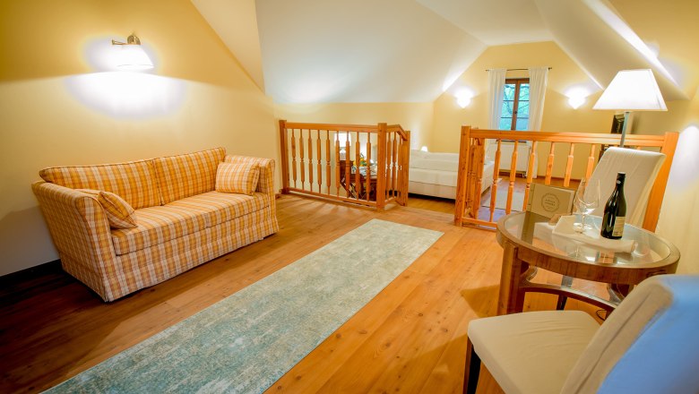 Cozy room with sofa, table and chair, wooden floor and railings.