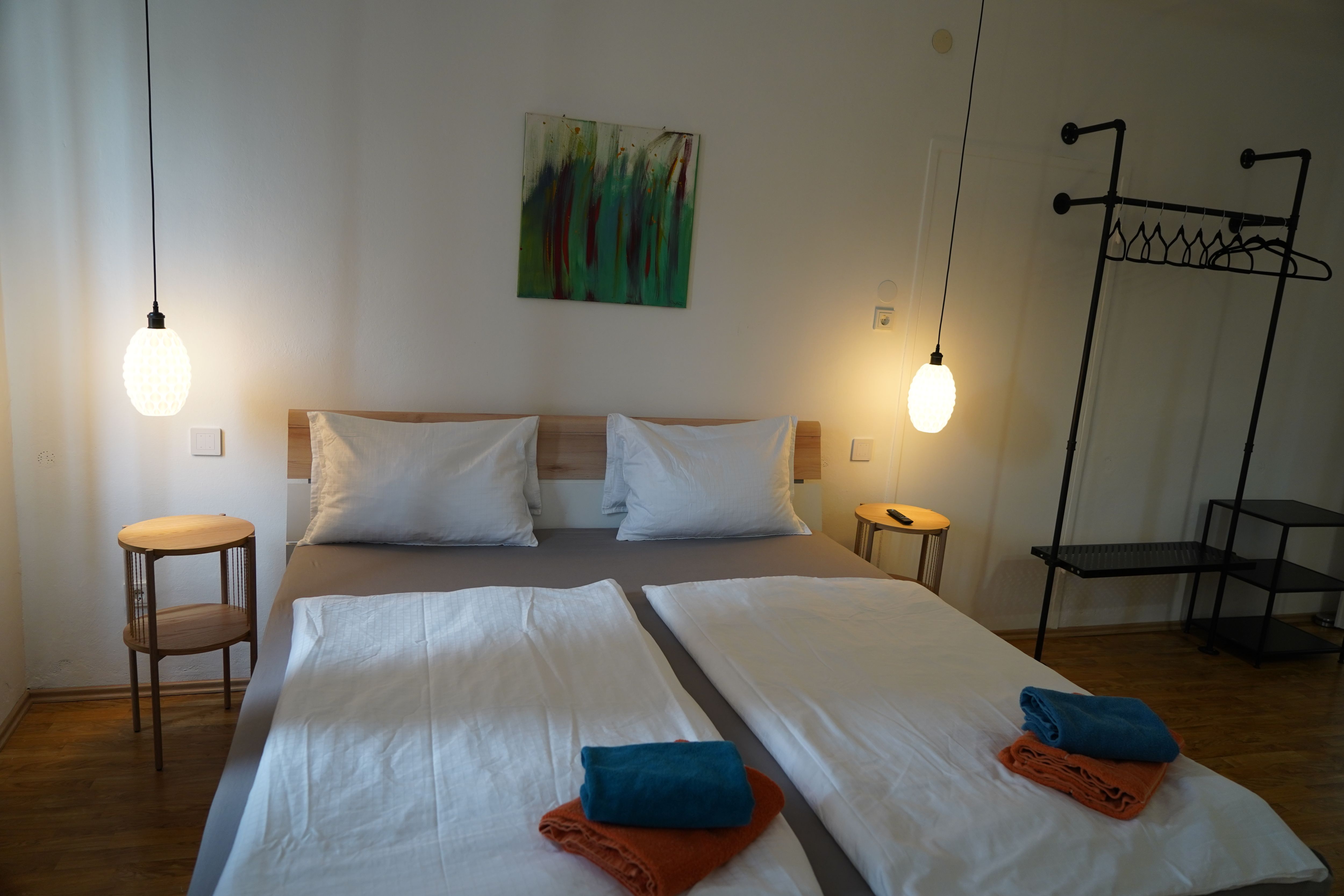 Modern bedroom with double bed, two bedside tables, hanging lamps and towels on the bed.