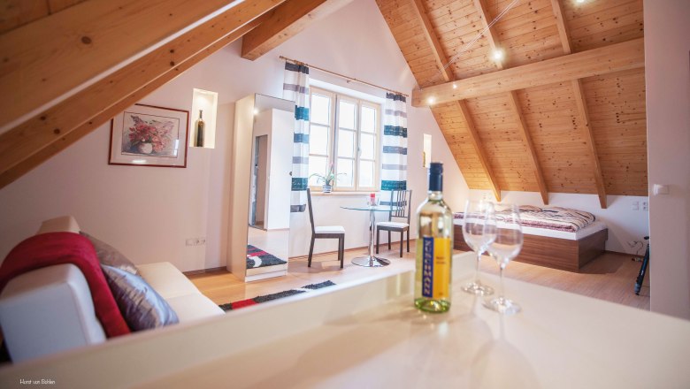 Zuschmann vicarage, © Horst von Bohlen Cozy attic room with wooden beamed ceiling, bed, sofa, table and wine bottle.