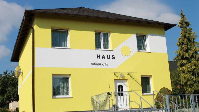 Yellow house with the inscription 'Haus' and a sun on the fa&ccedil;ade.