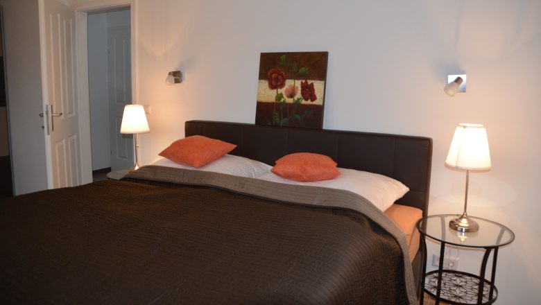 Bedroom with double bed, two bedside lamps and a painting on the wall.