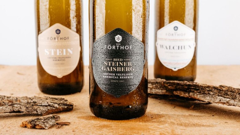 Three F&ouml;rthof wine bottles on a wooden table with pieces of bark.