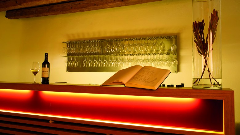 Wine tasting room with illuminated bar, wine glasses, a wine bottle and an open guest book.