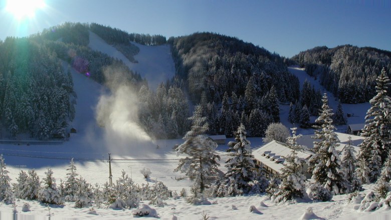 Snowy landscape with ski resort and sun in the background.