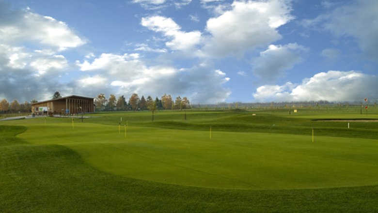 Golf course with clubhouse and cloudy sky.
