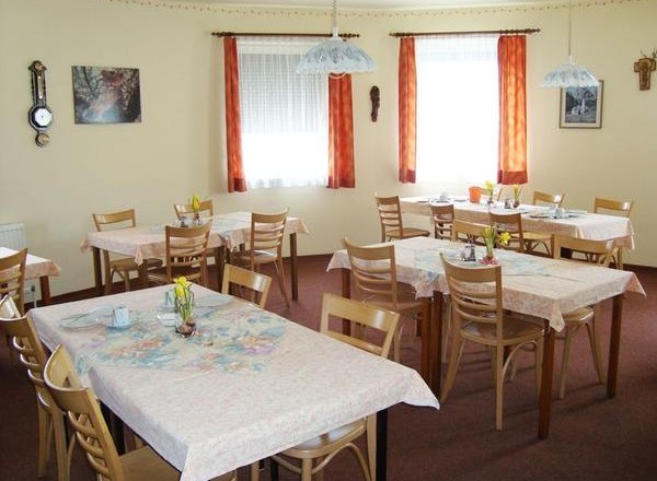 A cozy breakfast room with several set tables and wooden chairs, decorated with flowers and pictures on the walls.