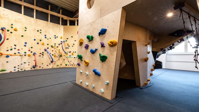 Interior view of a climbing hall with colorful climbing holds on wooden walls.