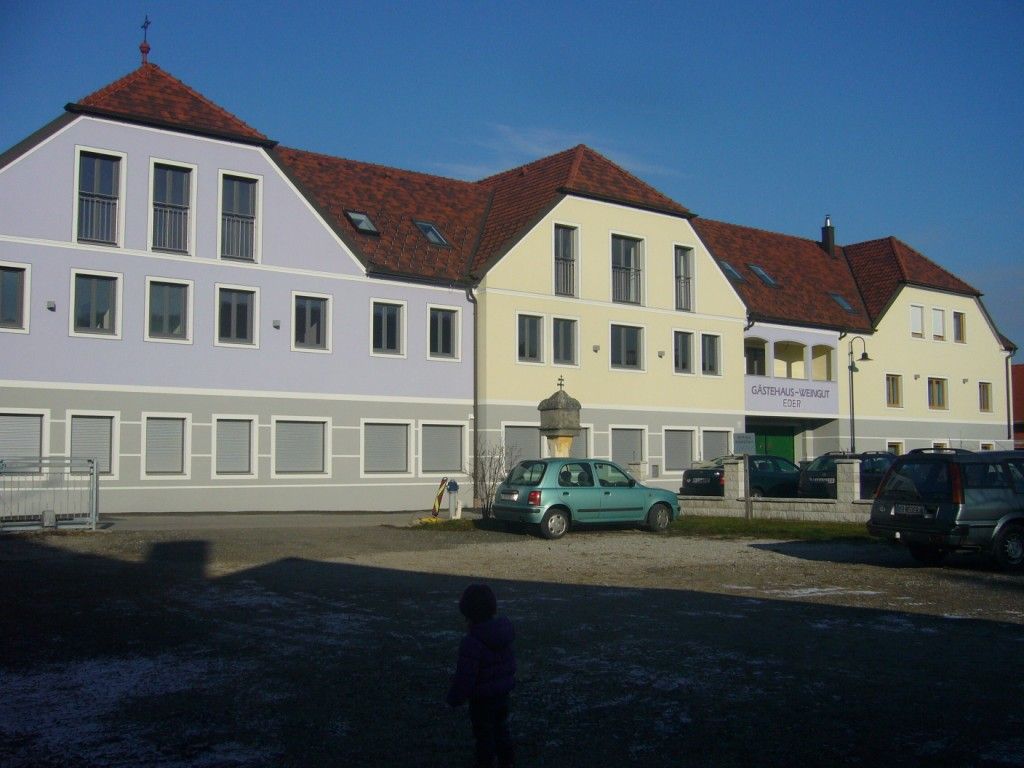 A modern guest house with red roofs and pastel-colored facades, cars in the foreground.