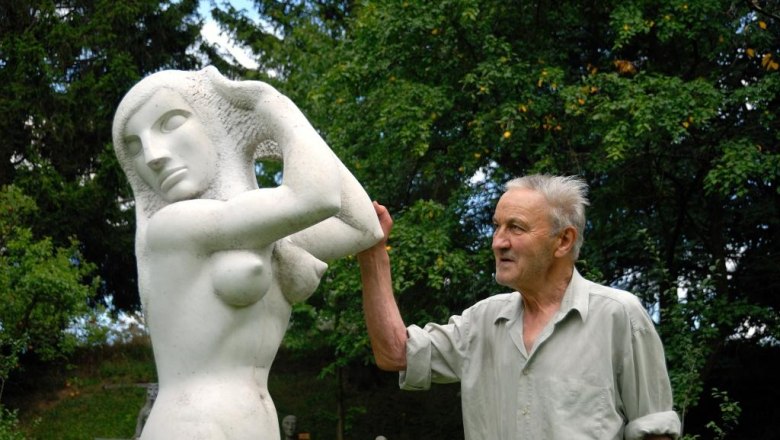A man stands next to a white sculpture of a woman outdoors.