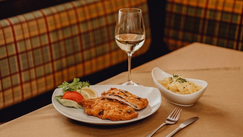 A plate of cordon bleu, salad garnish and a glass of white wine on a table.