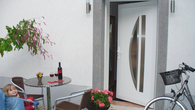 An open entrance with table, chairs, wine bottle and bicycle.