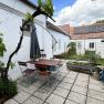 Terrace with table, chairs and grapevine on white wall, solar panel on roof in the background.