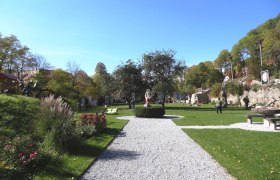A well-tended garden with sculptures and walkers in sunny weather.