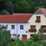 A traditional house with red roof tiles and flower boxes in front of the windows, surrounded by green vegetation.