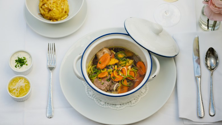 A table set with a stew in a white pot, a dumpling, two sauces and a glass of white wine.