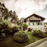 A villa with a green garden and trees in the background.