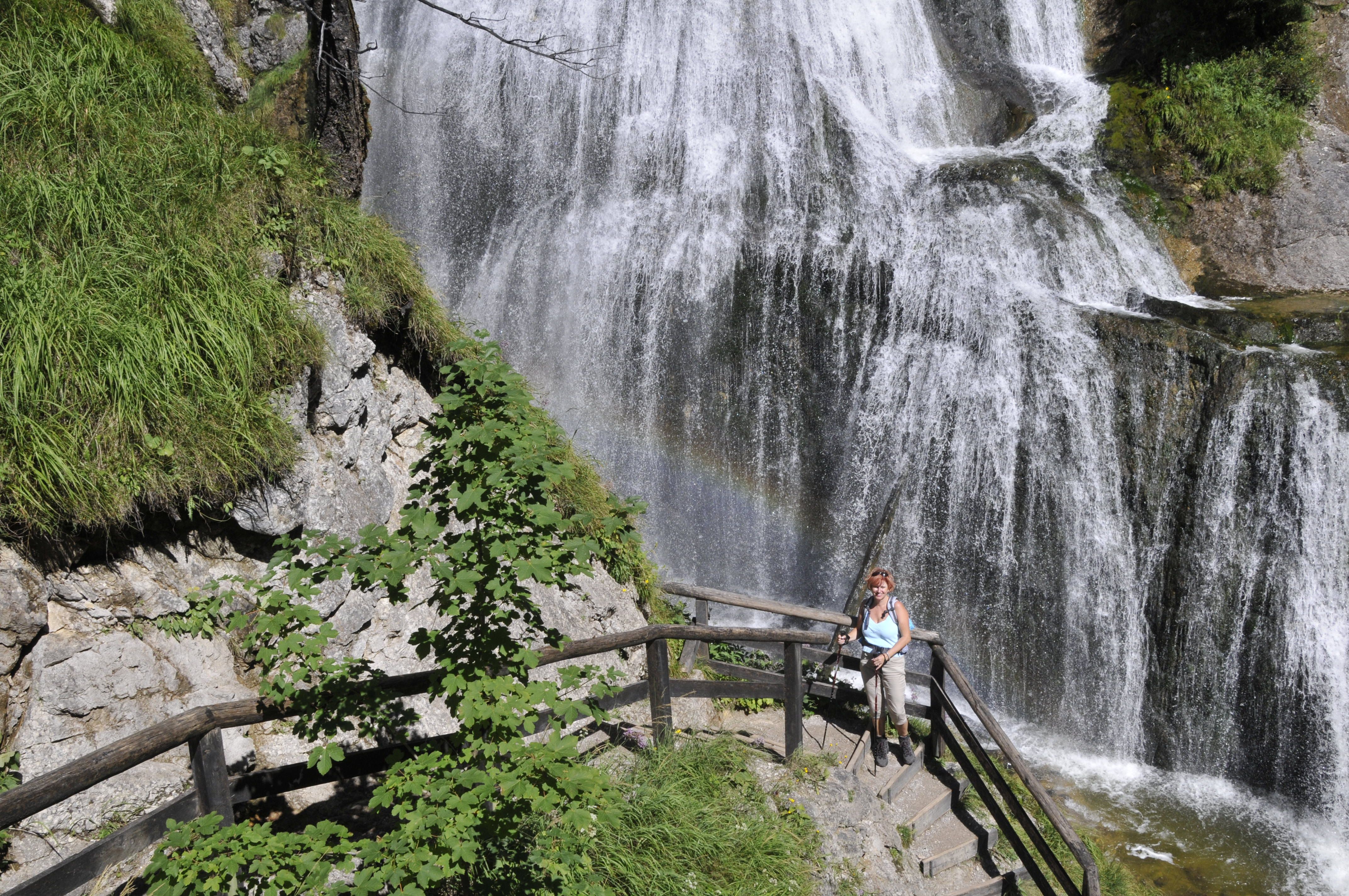 A woman stands on a staircase in front of a waterfall in the Palfau waterhole gorge.