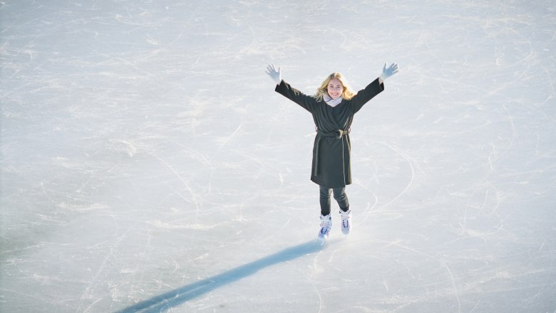 Person skating on an ice rink with raised arms.