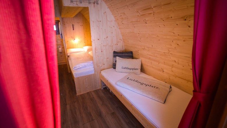 Interior view of a cozy wooden room with two beds and red curtains.