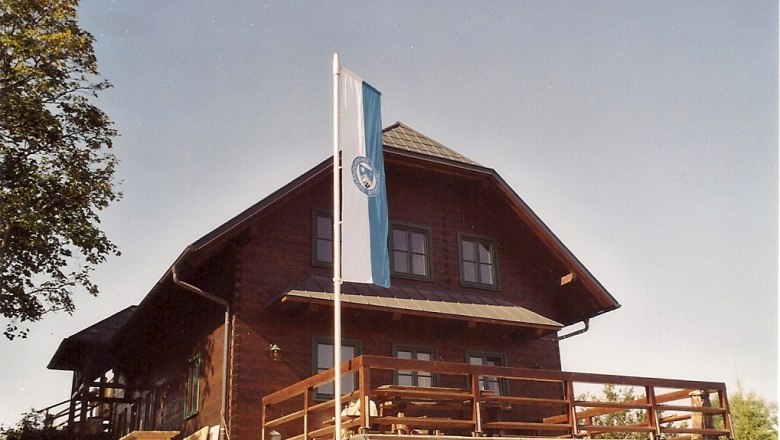 Wooden hut with flag on terrace, blue sky.