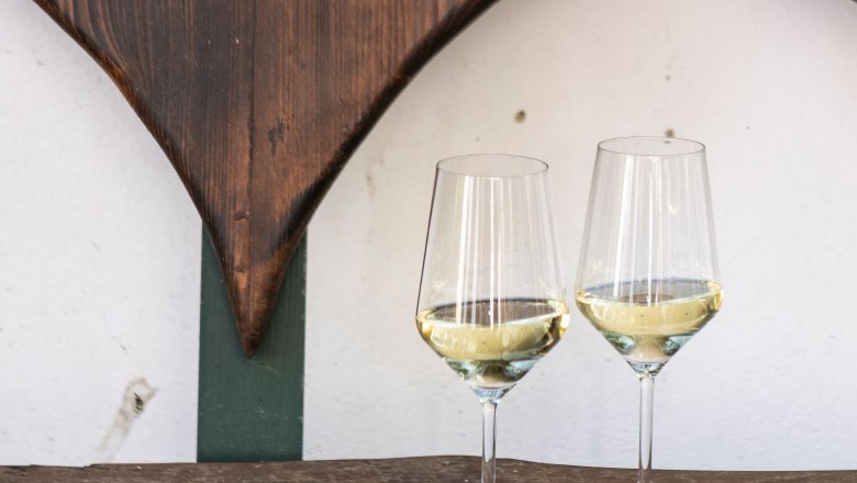 Two wine glasses with white wine on a wooden table in front of a wooden heart decoration.