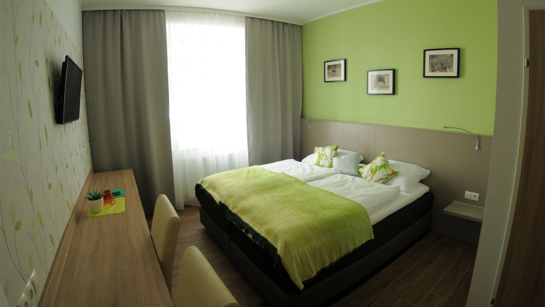 Modern guest room with green color scheme, double bed, desk and wall decorations.