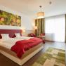 Modern hotel room with double bed, red ceiling, wooden furniture and large window. A picture of fruit hangs on the wall.