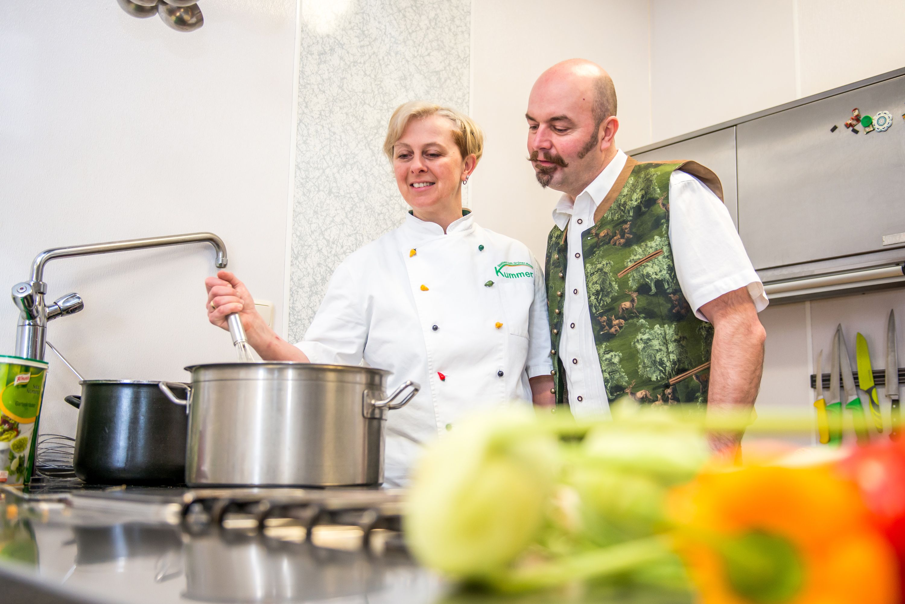 Two people in a kitchen, one stirring a pot, the other watching.