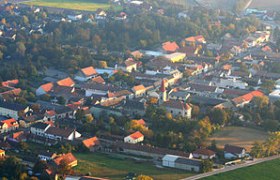 Aerial view of a village with church and houses, surrounded by trees and fields.