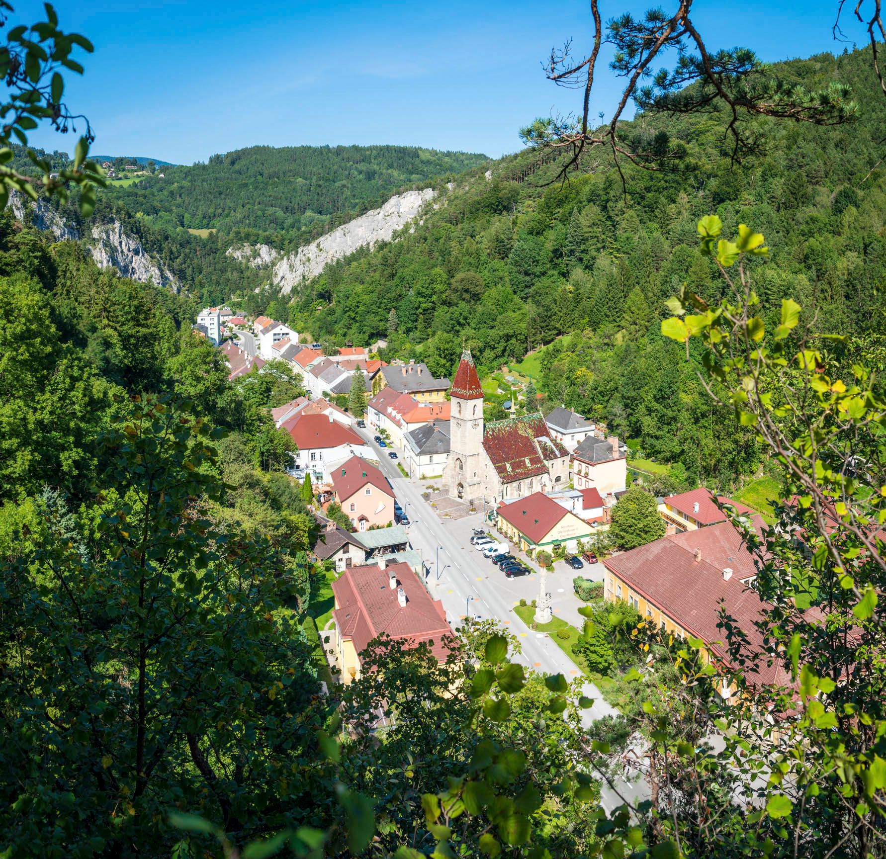 Aerial view of Schottwien with church and surrounding buildings, surrounded by wooded hills.