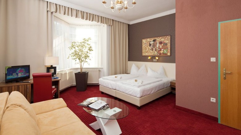 Hotel room with double bed, red carpet, sofa, TV and large window.