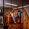 Children play in an indoor climbing area with wooden walls and colorful climbing holds.